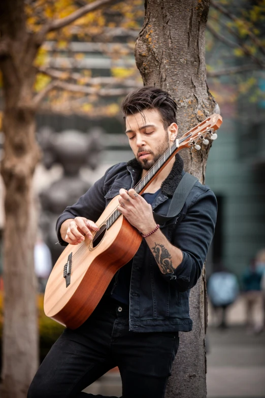 a man playing a guitar in front of a tree
