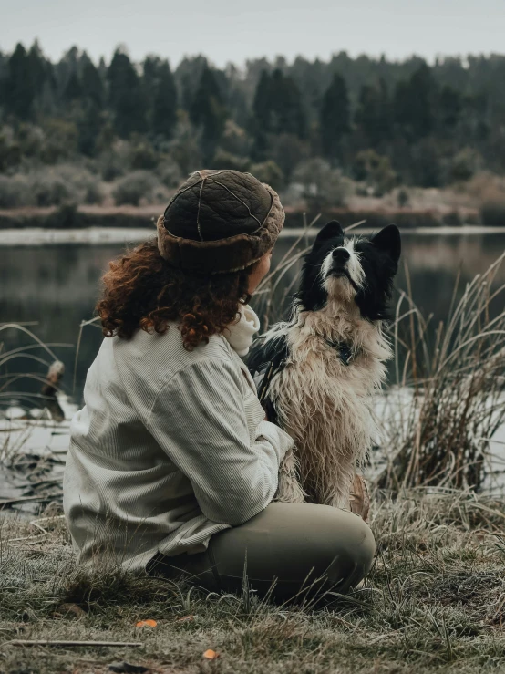 a woman is sitting near a lake with her dog