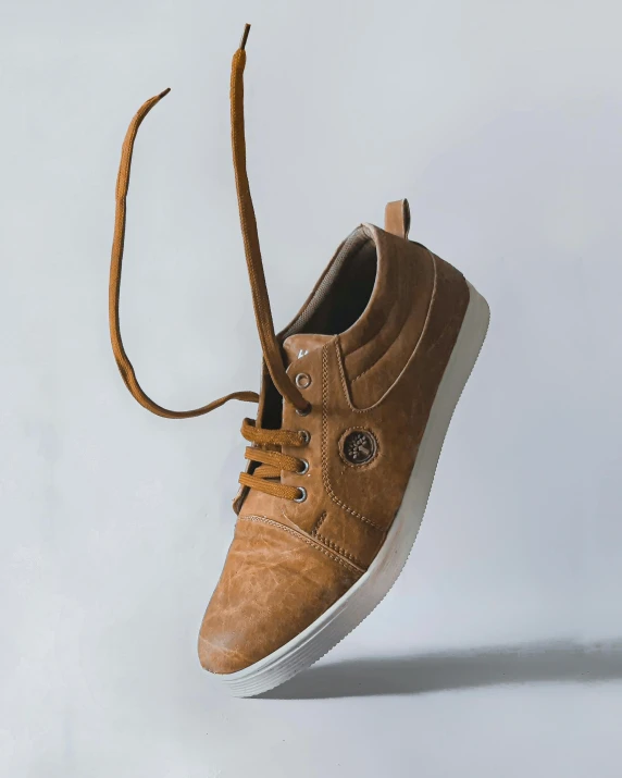 a brown sneaker that is very sharp and has a ribbon around the toe