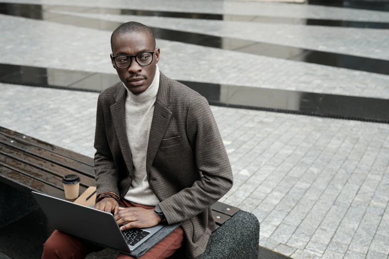 an african american man sitting on a bench, using his laptop