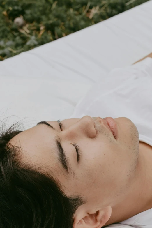 a man laying on a white sheet with a sleeping cat