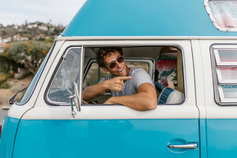 man with sunglasses on smiling out the window of an old blue and white van