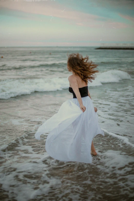 a woman with a flowing white dress walking on the shore line