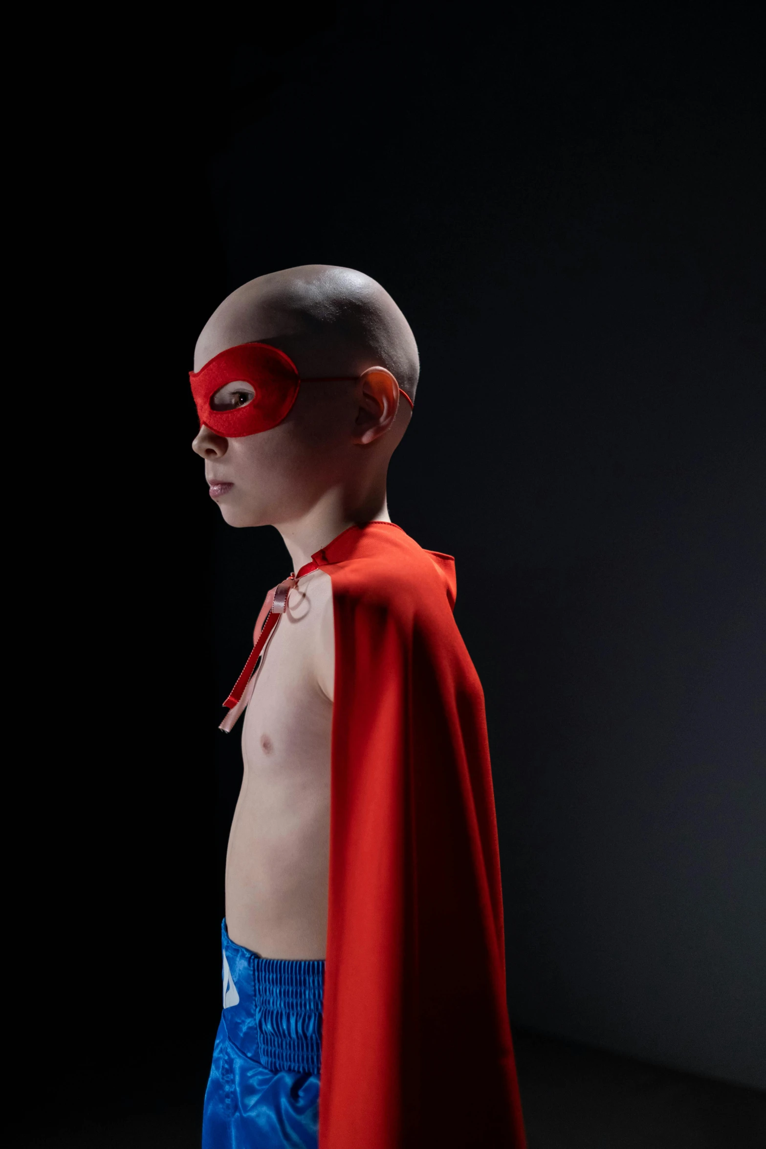 a boy in superman cape and mask poses in dark