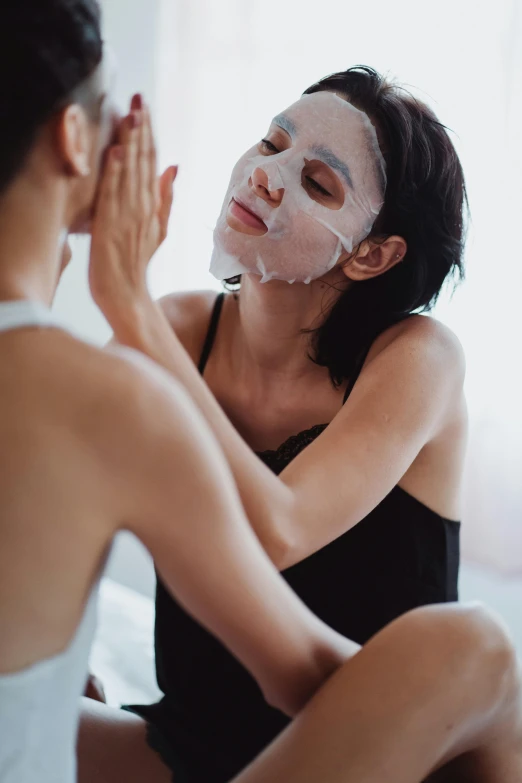 two women in a spa setting, one applying their face