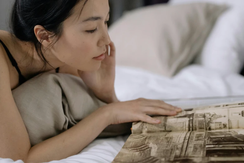 woman in grey shirt reading magazine on bed