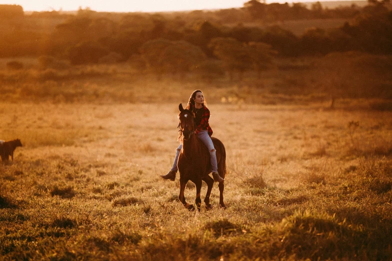 a woman riding on the back of a brown horse through a grass covered field