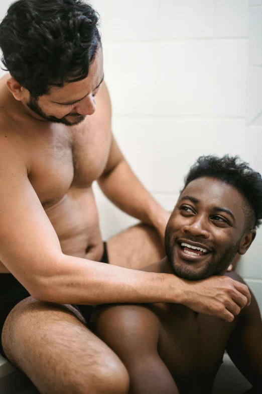 man sitting on toilet with another man standing by and looking at him