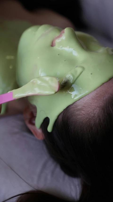 woman has a green substance on her face with pink spoon