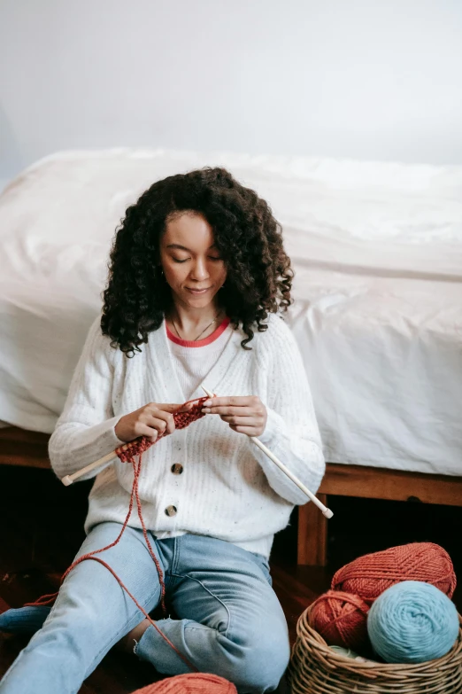 a woman knitting with two skeins of yarn in front of a bed