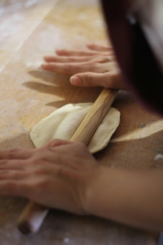 hands knead dough on a counter top and a paddle in the middle