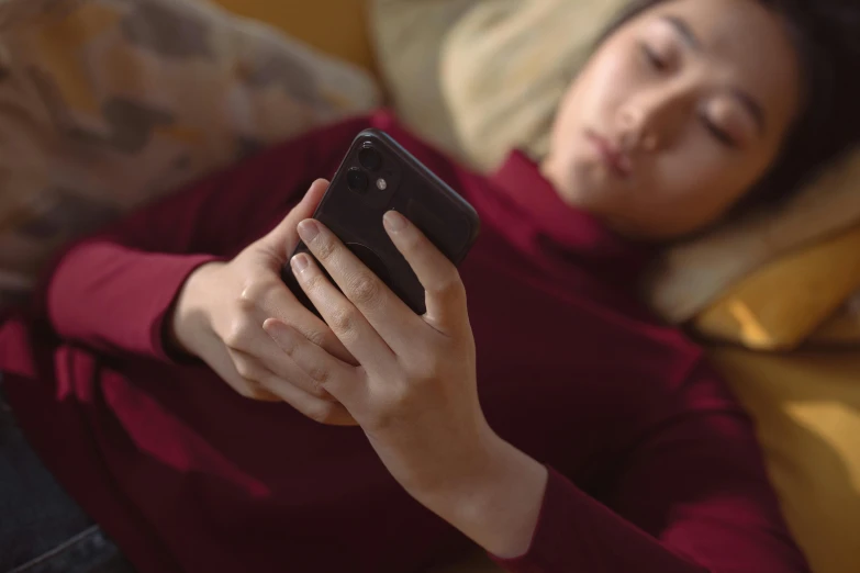 a girl with a red top is laying down on a sofa and looking at her phone