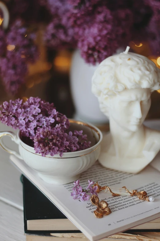 a cup of flowers sits next to an open book on a white table