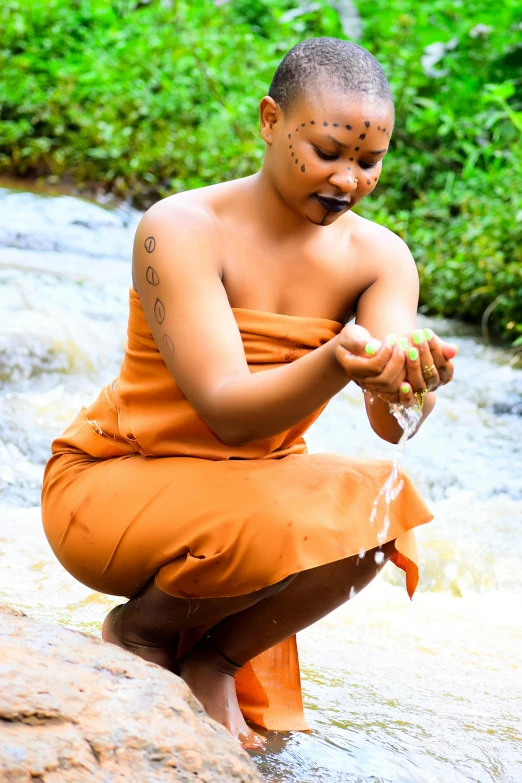 a man with his face tattooed is sitting by a stream holding a piece of food