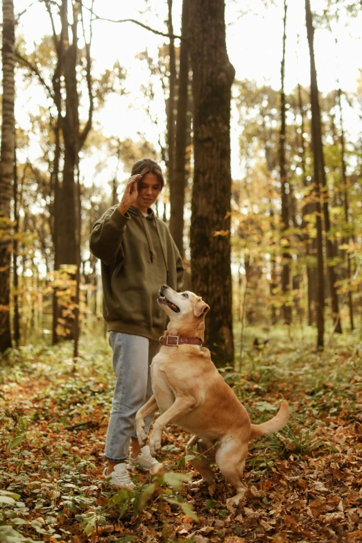 a man in the woods talking on a cell phone while his dog jumps into the air