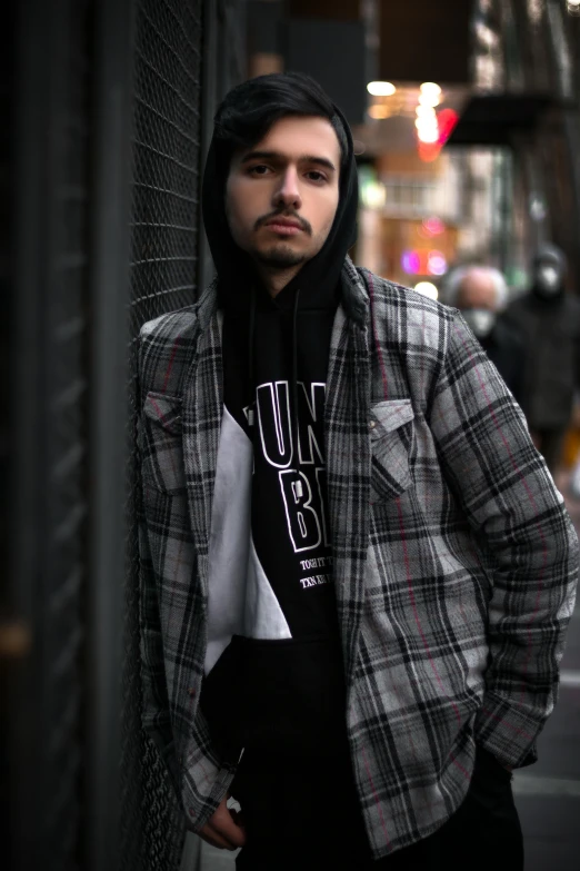 a young man leans against a wall on a city street