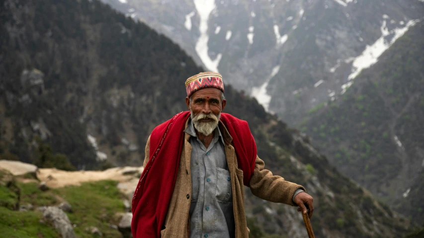 a man with a long beard wearing a red blanket and carrying a stick