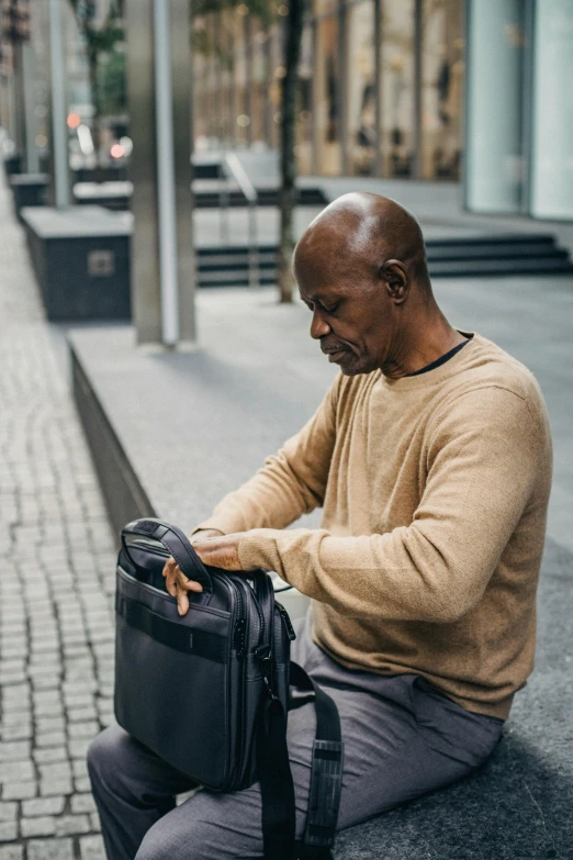 an older man sits on the sidewalk with his back pack