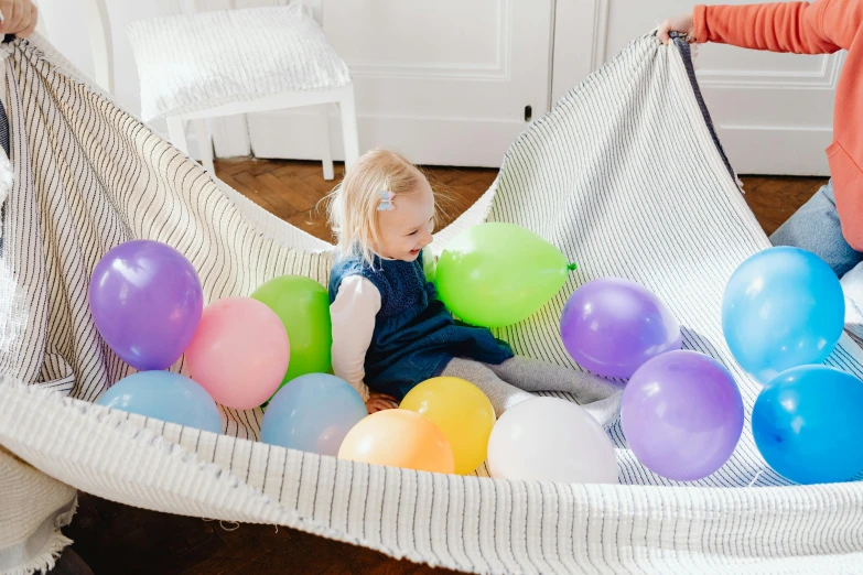 the little girl is laying in a ball pit with balloons