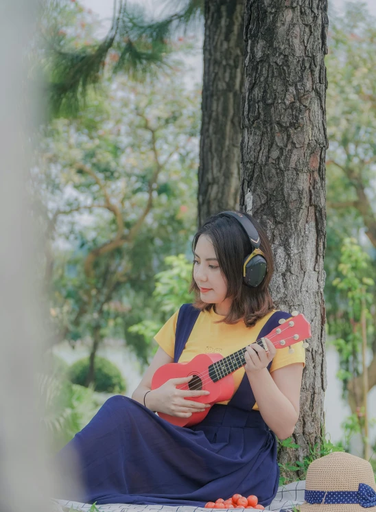 the girl is sitting under a tree with an acoustic guitar