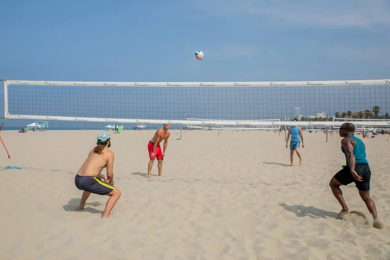 two teams of men and women play volleyball in the sand