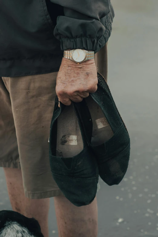 someone holding on to their leather shoes while wearing one with an automatic watch