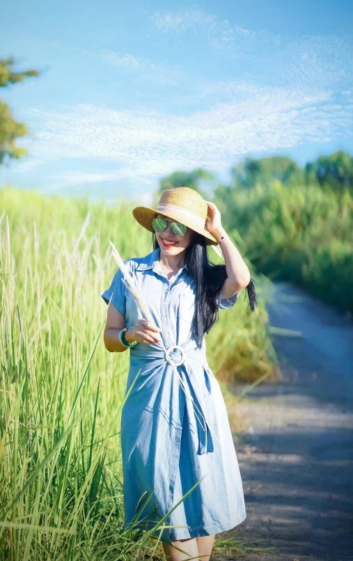 a young woman wearing sunglasses and a sun hat stands near a grassy path