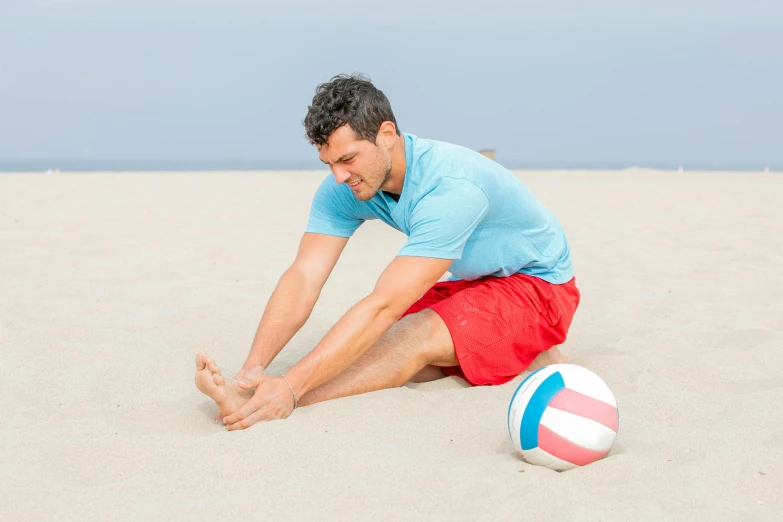 a man sits on the beach and holds his feet up as he has a ball