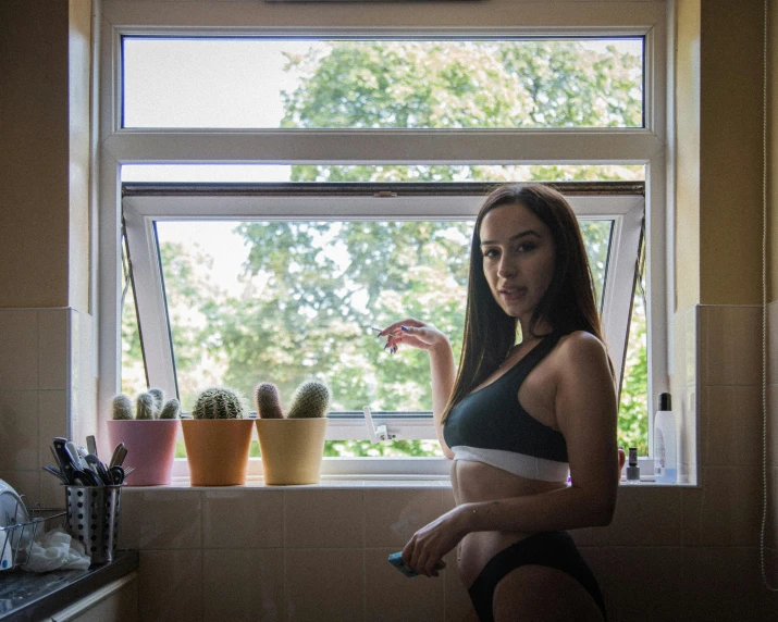 a woman looking out the window, standing in front of a kitchen window with pots and panes of cactus on the windowsill