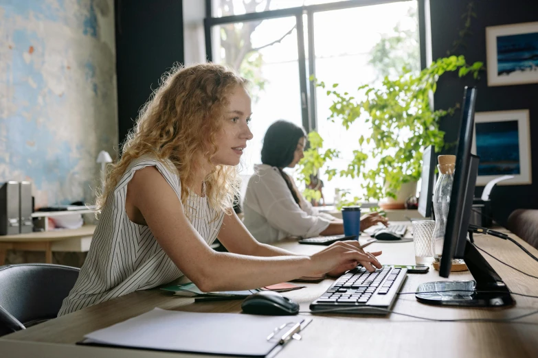 woman with long hair sitting at desk typing on computer