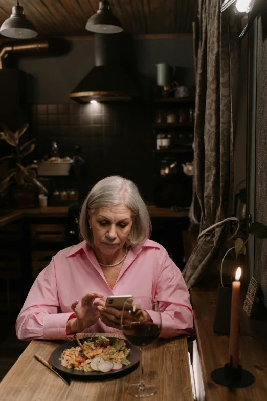 a older woman sitting in front of a meal while looking at her phone