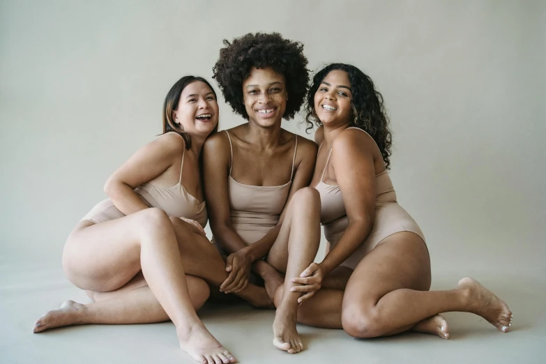 three women in tan underwear sitting on the ground smiling