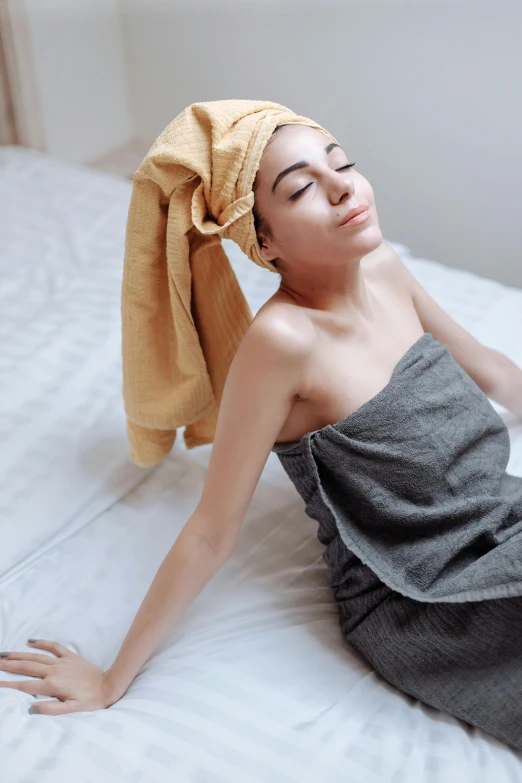 a young woman lays on a bed and covers her face with towels