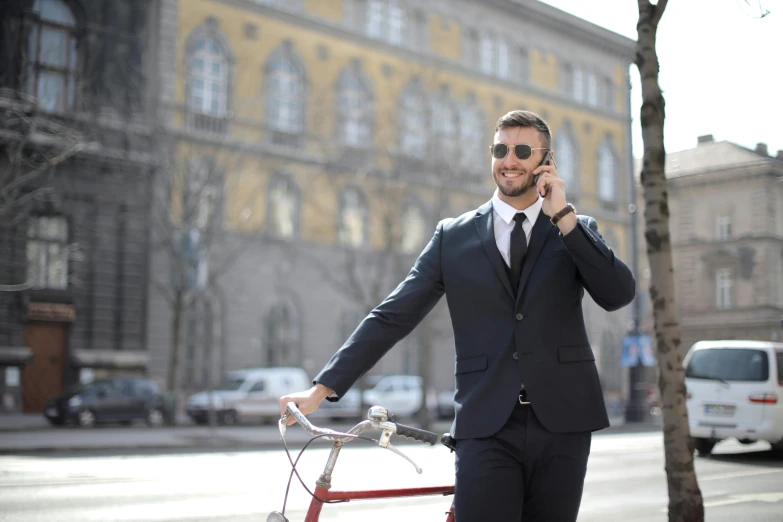 a man in business attire on the phone and standing by a bicycle