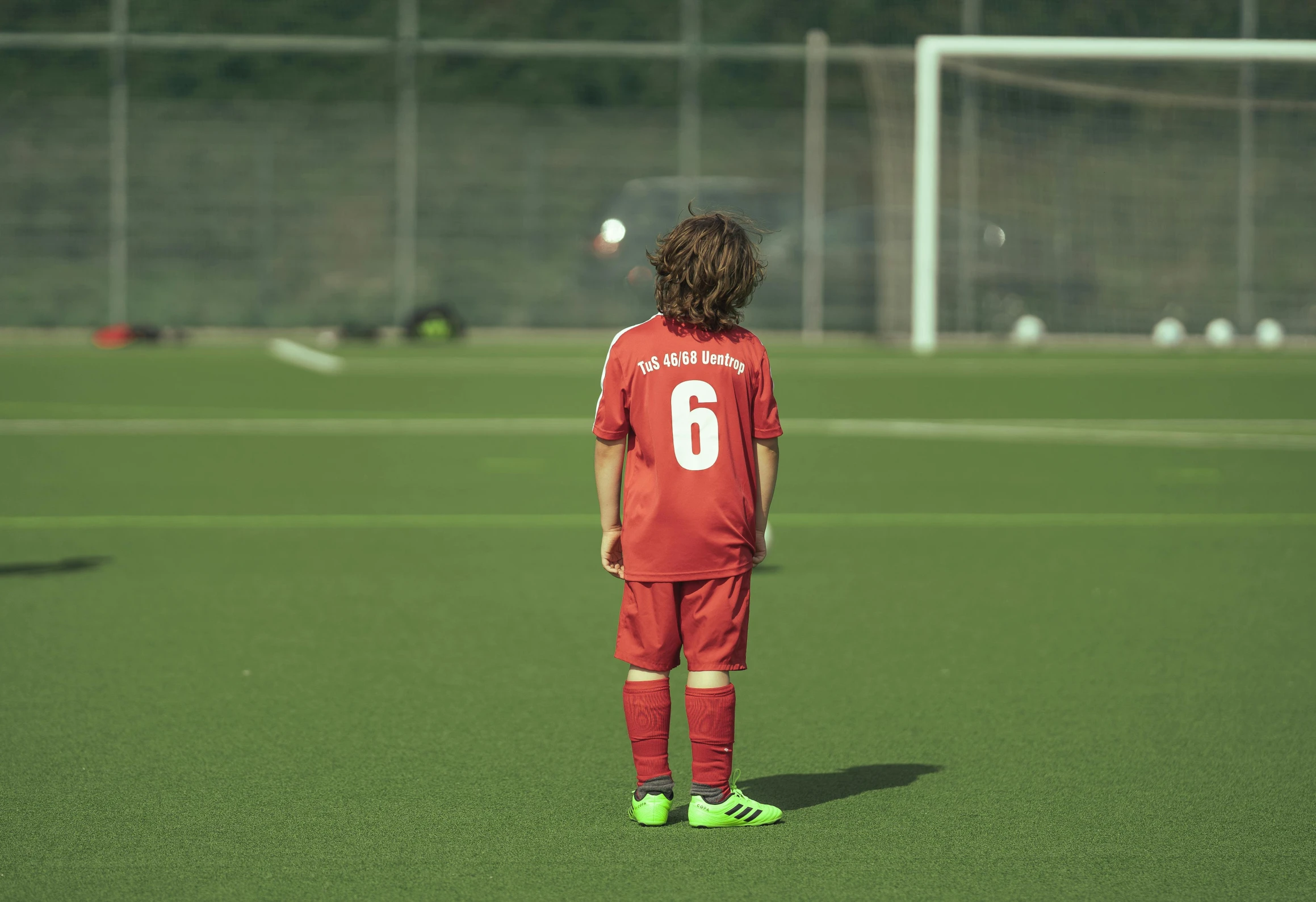 young child standing on soccer field with ball on field behind him