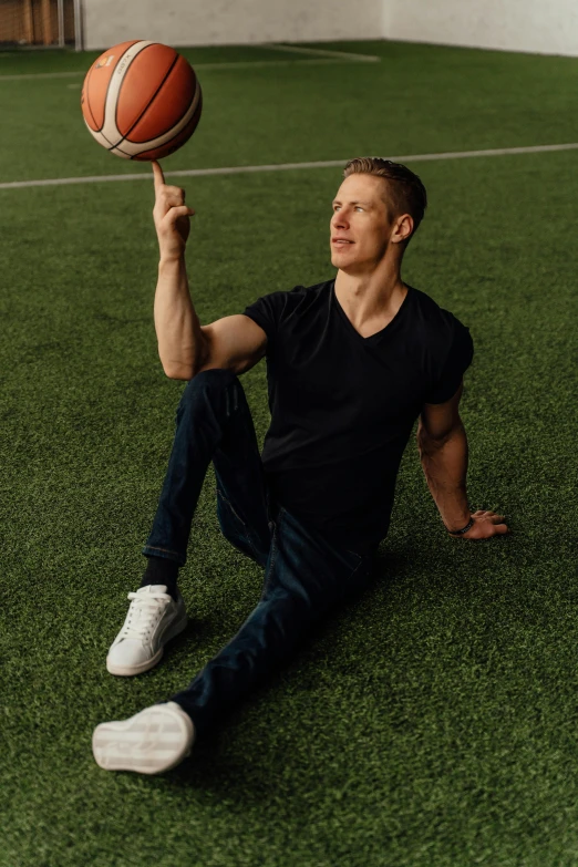 a man sits in the grass, holding up a basketball