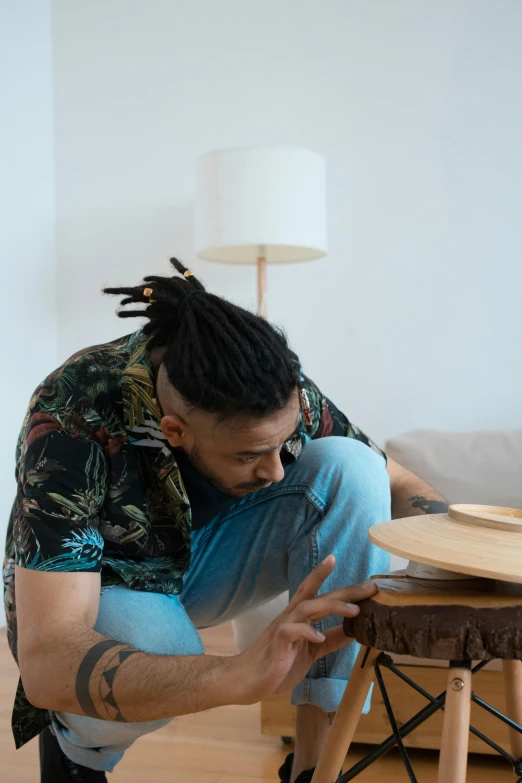 a man squatting on the floor near a wooden table