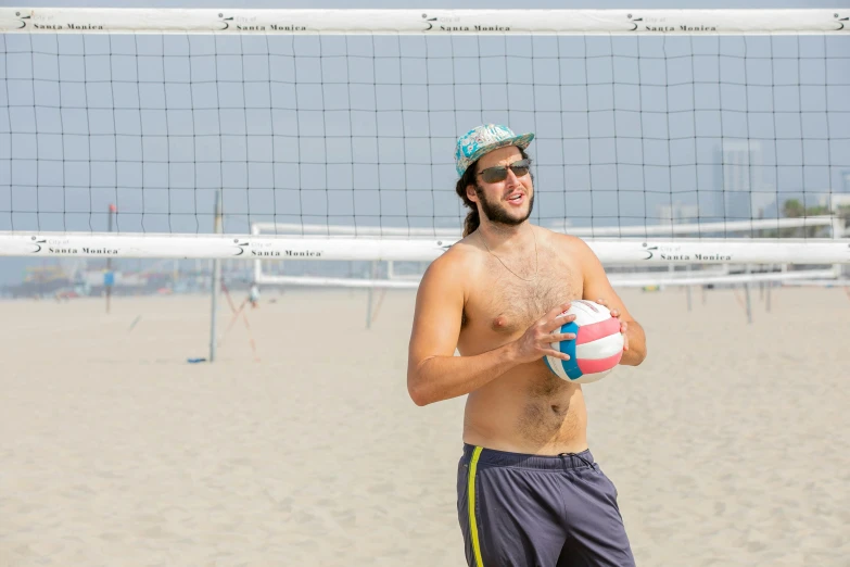 a shirtless man holding a volleyball ball on the beach