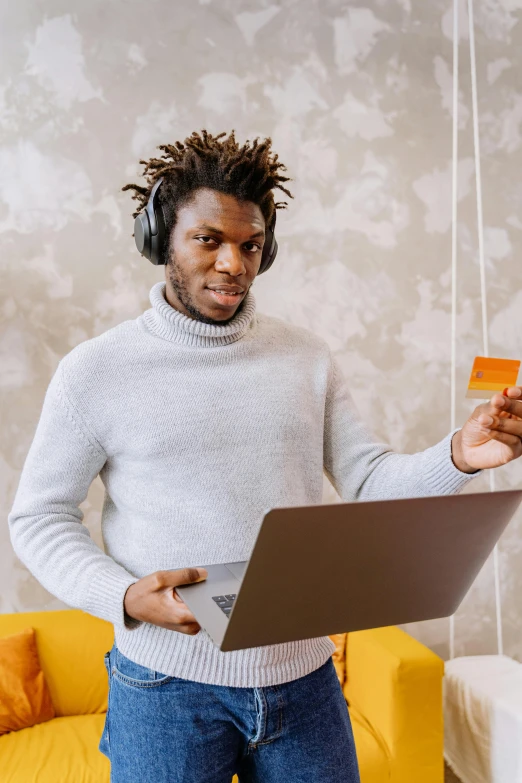 a man stands next to a laptop holding a credit card