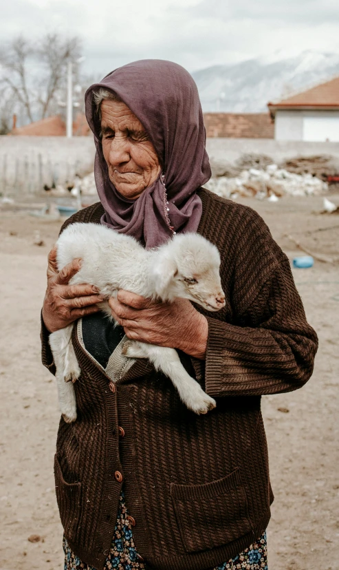 a woman with a brown jacket is holding a white sheep