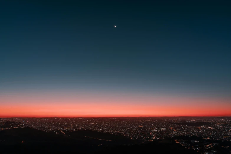 an orange sky with white crescent above and some lights