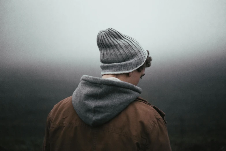 a man in a hat, jacket and scarf looks down at the fog
