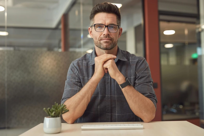 a man with glasses at a desk with his arms folded up