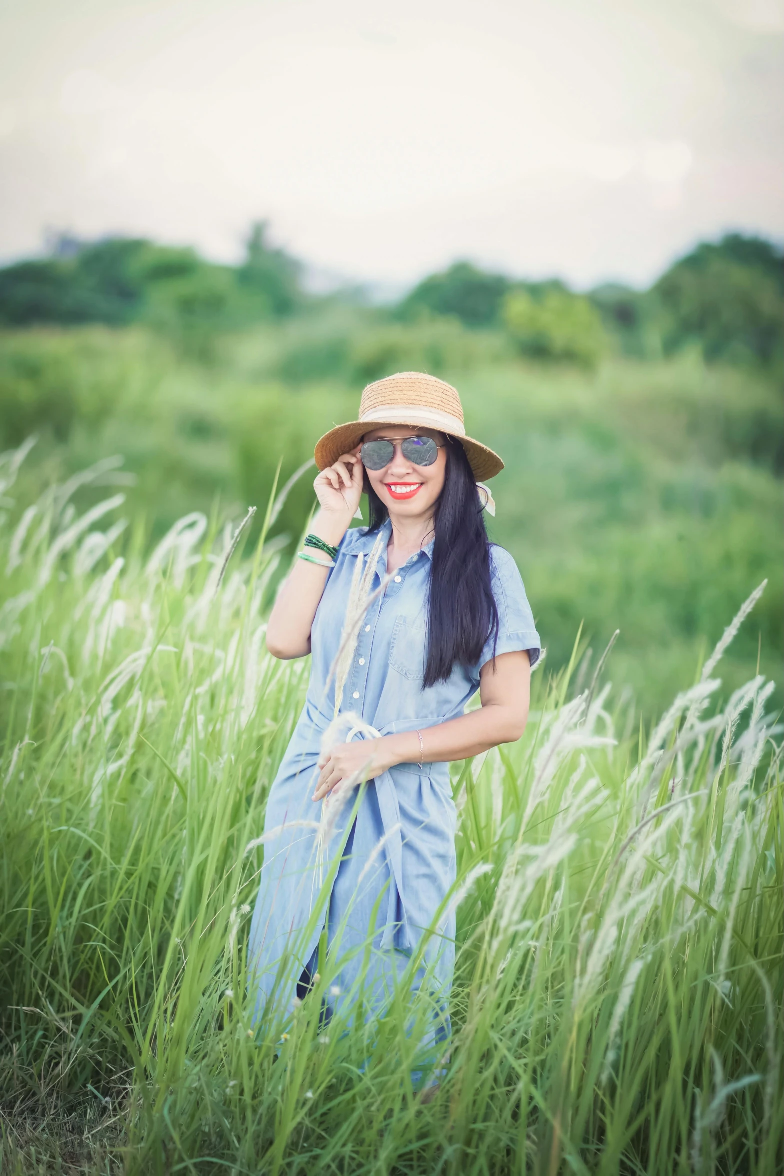 a woman in a hat and glasses posing in tall grass