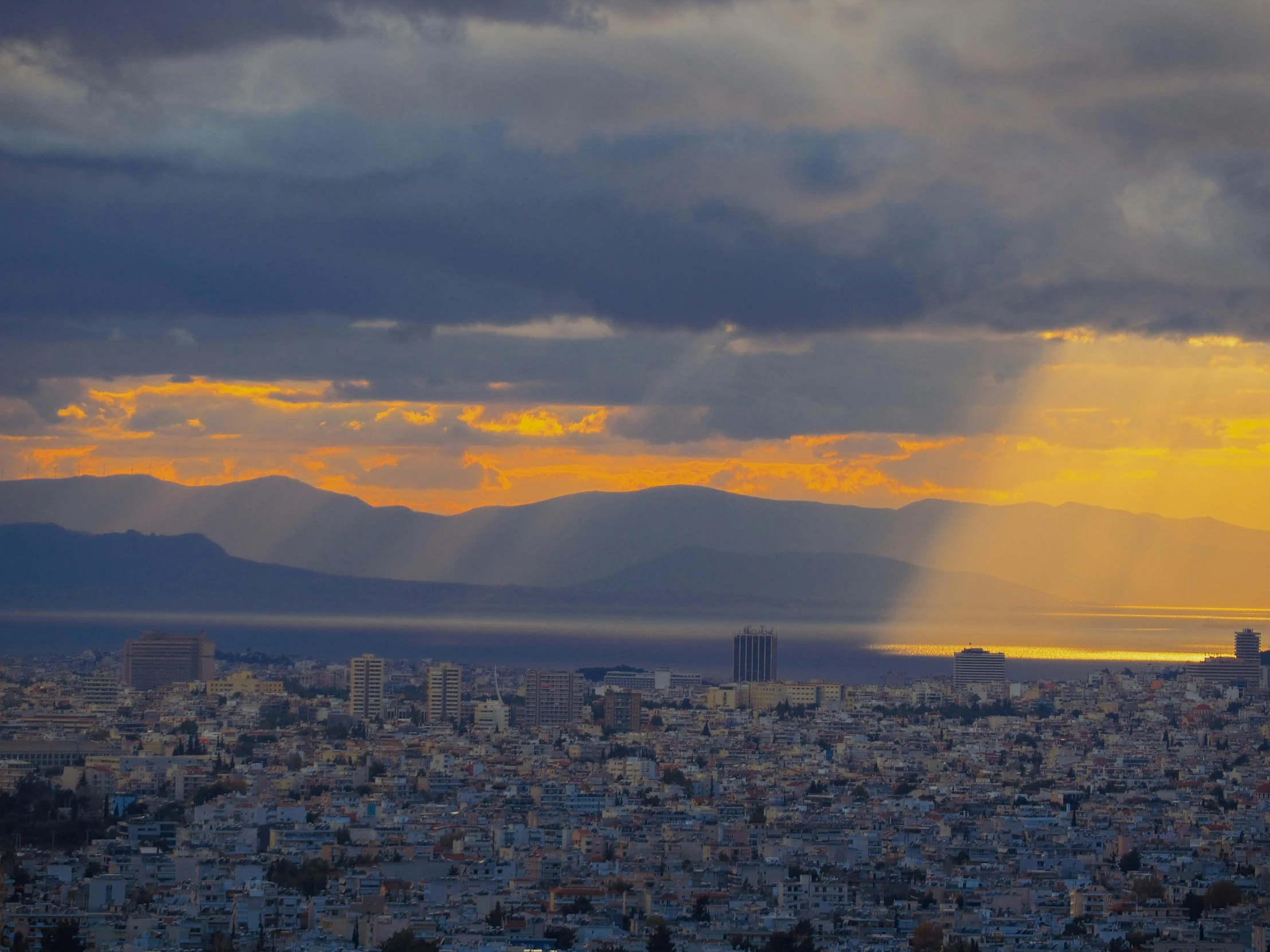 sunset behind a city under cloudy skies and mountains