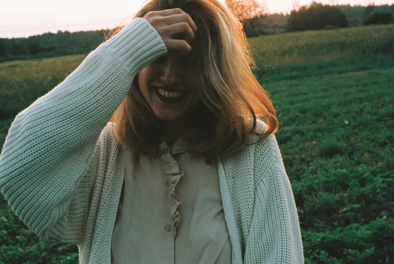 a woman in a field of grass wearing a sweater