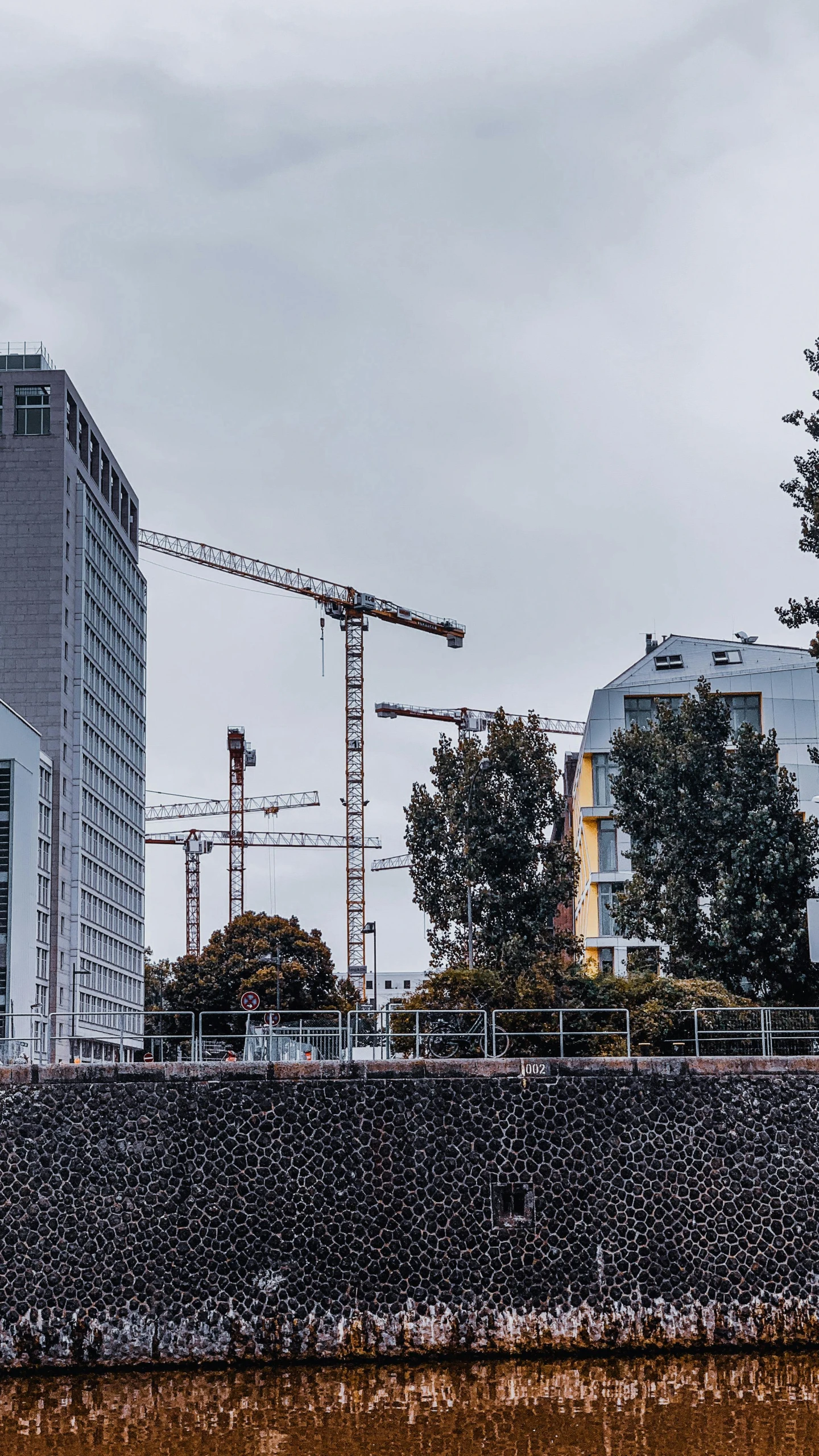 a group of cranes and some buildings under cloudy skies