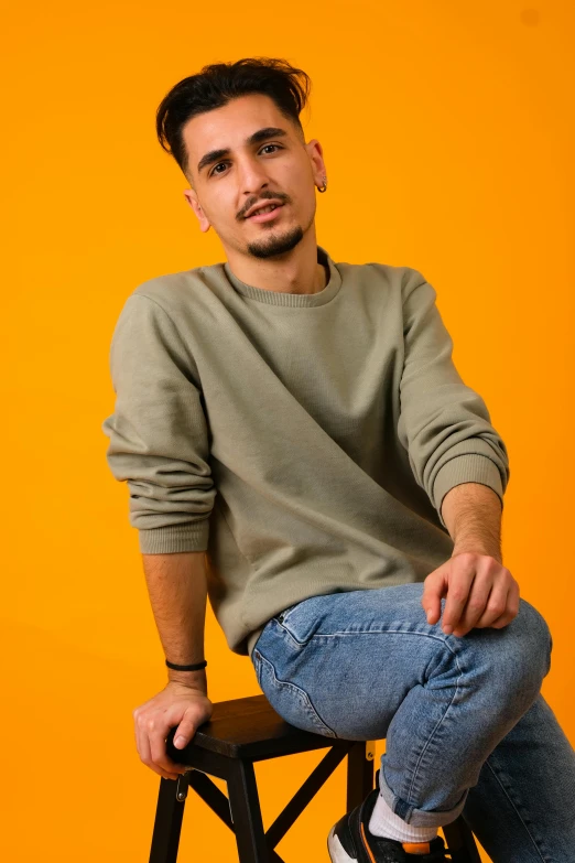 a man wearing a sweater and blue jeans is sitting on a stool