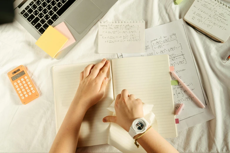 a woman is sitting in front of her laptop writing in a notebook