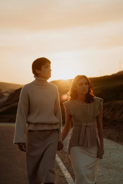 two people are walking on a road, at sunset